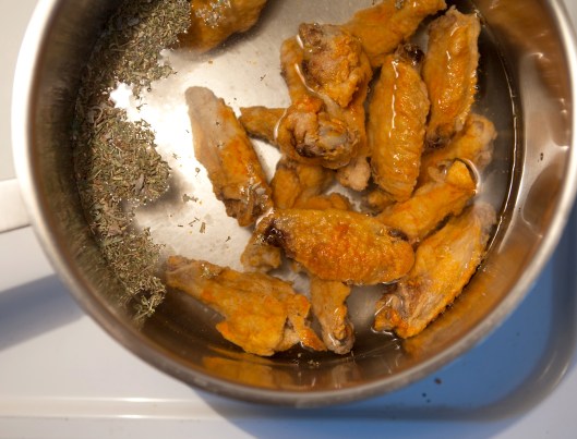 Place hot chicken wings and a handful of fresh or dried herbs in a couple quarts of water in a pot.